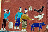 Wat Xieng Thong temple in Luang Prabang, Laos.  La Chapelle Rouge , the Red Chapel. The exterior walls are decorated with colourful mosaics on a pink background with scenes of people daily activities. West wall. 